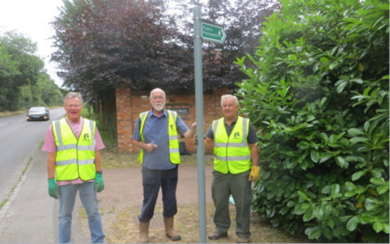 Three volunteers in high viz waistcoats next to a footpath sign