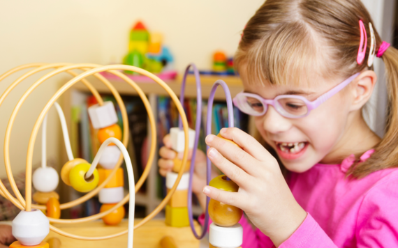 A girl smiles widely while playing with a bead run