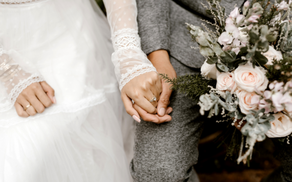 A close-up of a wedding couple holding hands
