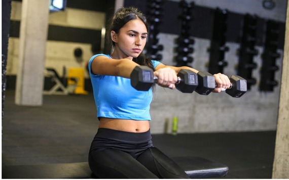 A girl lifts two dumbbells in front of her using her shoulders