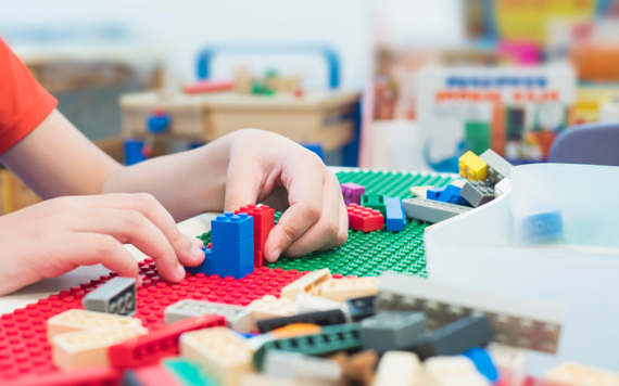 A child's hands building a red tower and blue tower out of lego