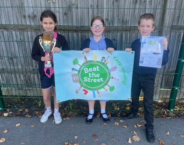 Three children holding a trophy and posters for Beat the Street competition