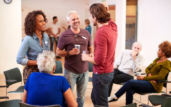 Group of people stood chatting and drinking coffee 