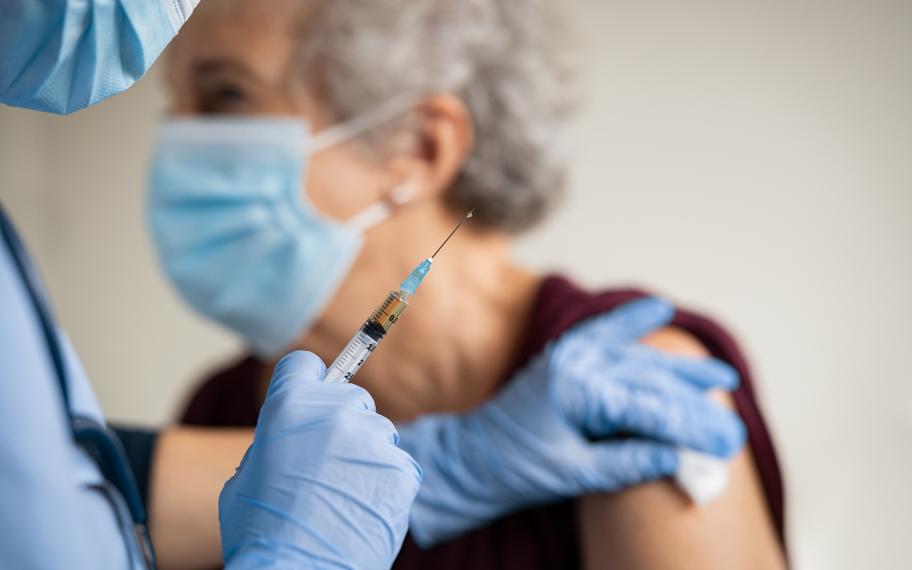 A nurse prepares a vaccine to go into the arm of an older woman