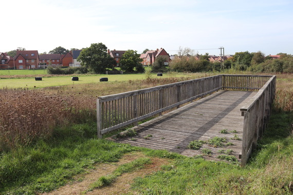 A wooden viewing platform overlooking a landscaped nature park consisting mostly of a grass field