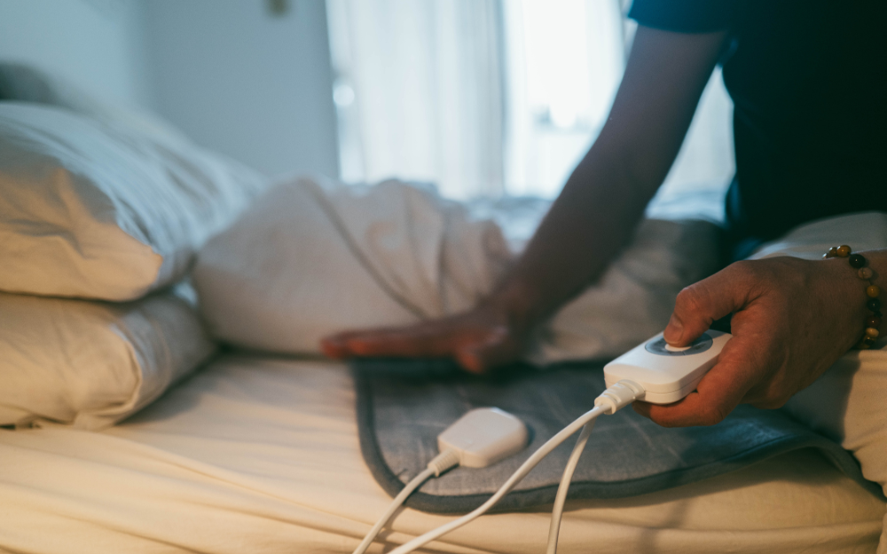 A person pressing the button on an electric blanket on a bed