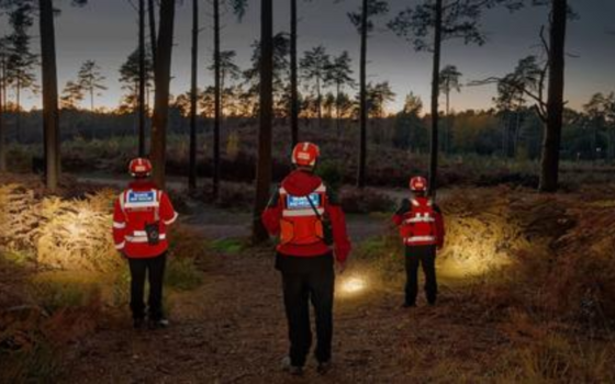 Three berkshire lowland rescue volunteers searching a woods by torchlight