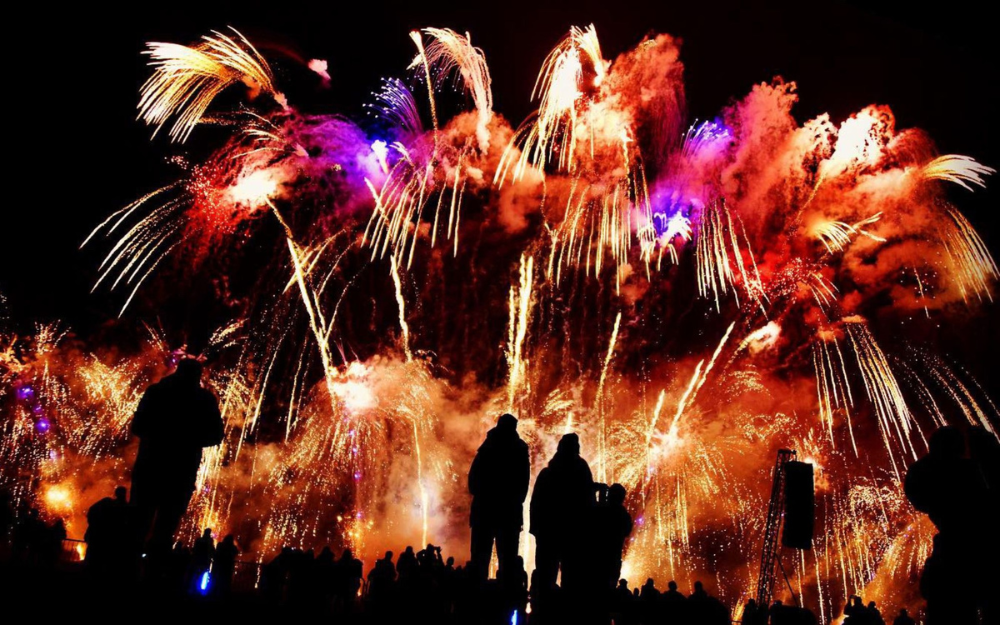 A huge, colour fireworks display towers over people watching on