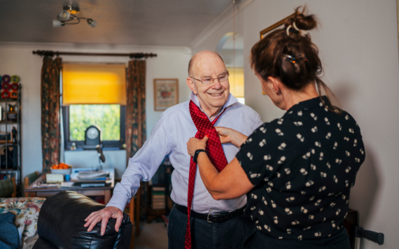 Lady helping an older man to put on his tie in his home