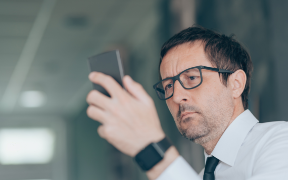 A man wearing shirt and tie holds up his phone looking at it