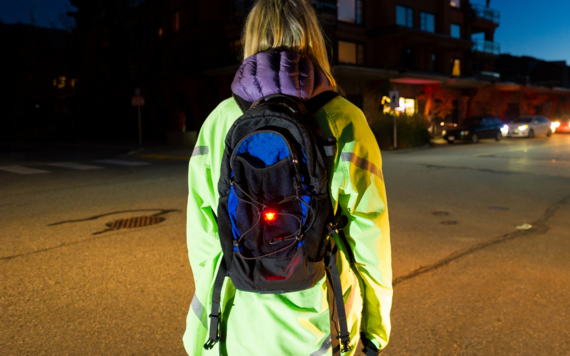 A person standing taken from behind wearing a high viz coat and a light on their backpack