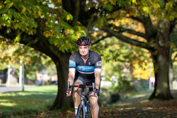 A male on a bike riding through a park wearing cycling lycra and helmet