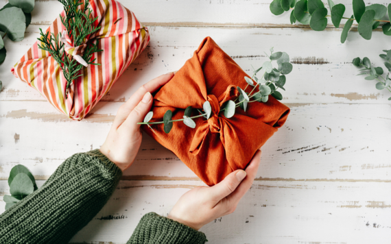 A top view of hands holding a gift wrapping in cloth decorated with a sprig of a plant