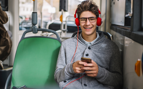 A teenage boy travelling on the train, wearing headphones and smiling