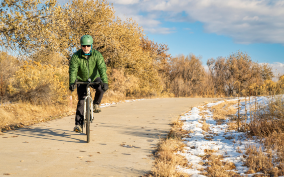 Person wrapped up warm cycling along path with melting snow in the grass