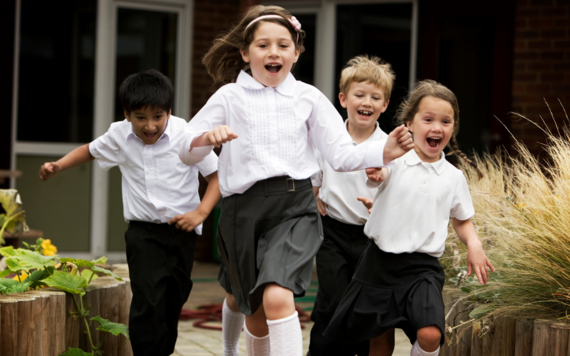 Picture of four school children in uniform running forward with excited looks on their faces