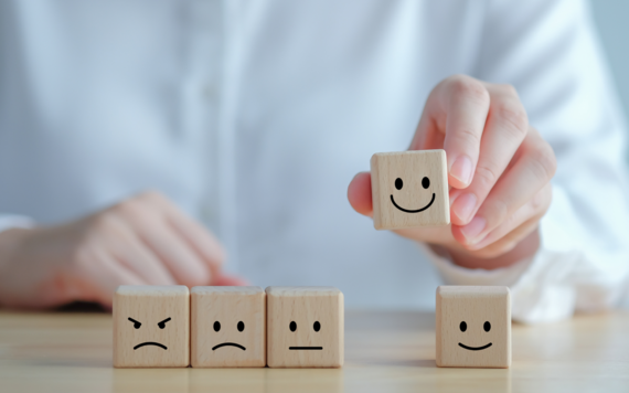 Five wooden die each have a facial expression on. A man lifts a 'happy face' die.
