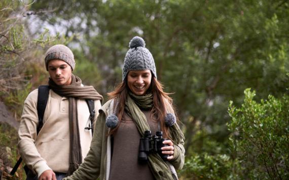 A young man and a woman walking in the outdoors with binoculars