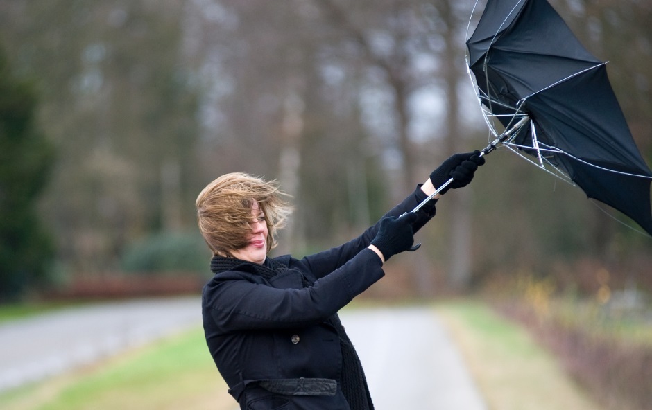 A woman struggling with an inside-out umbrella and messy hair on a very windy day