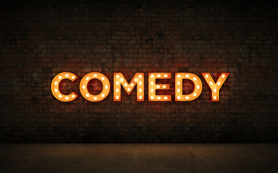 A neon sign that reads COMEDY on a brick wall background