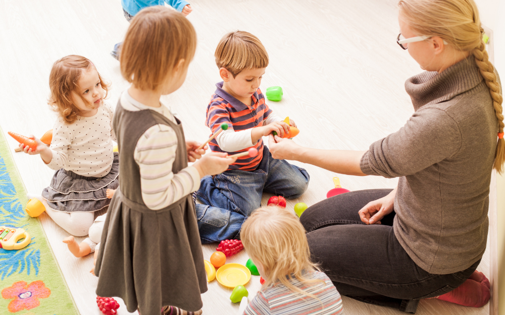 A play worker with four children on the floor at a nursery
