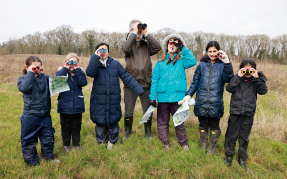 Pupils holding a binocular and watching birds with an ecologist