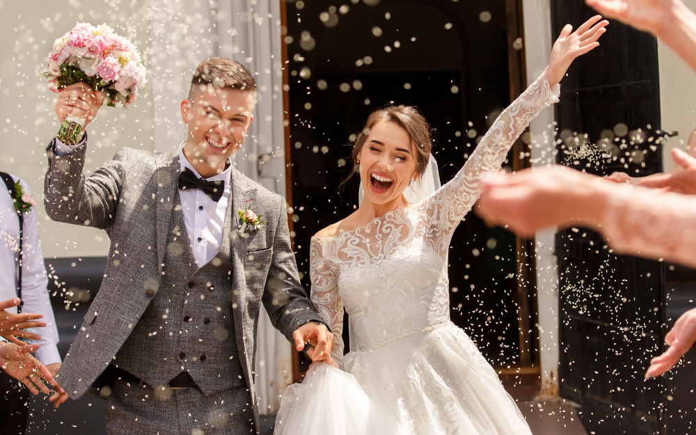 A bride and groom beam as they are showered with confetti