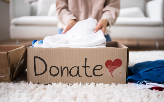 A close up of clothes being put into a box that read Donation in the front 
