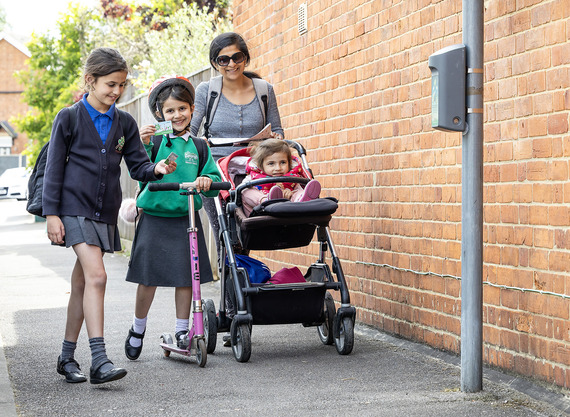 A mother and young children, including one in a pushchair, walk down a pavement to touch a score card to a reader