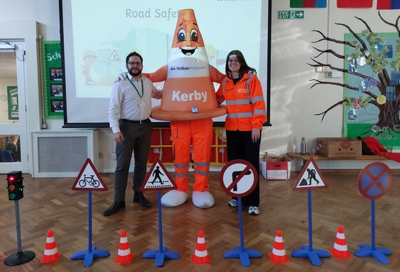 a mascot dressed in a cone costume giving a school assembly, with miniature road signs in front of them