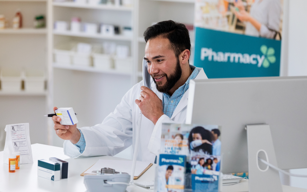 A pharmacist working behind a counter, on a phone and arranging medication