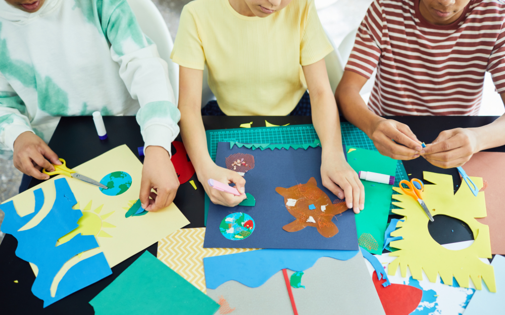 Children creating art on a table using paper and scissors