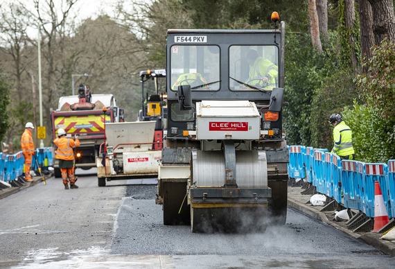 a steamroller driving over a new layer of freshly laid tarmac