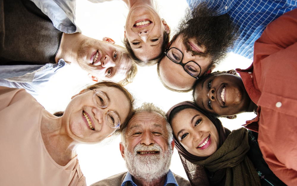 A mixed group of people with their heads in a circle smile to the camera