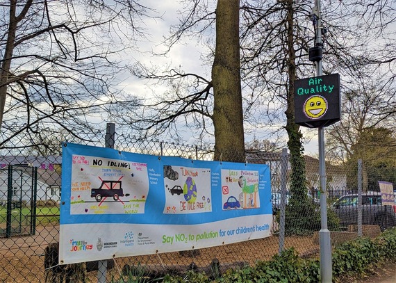 A display screen attached to a lamppost outside a school, showing a smiley face under the words "air quality"