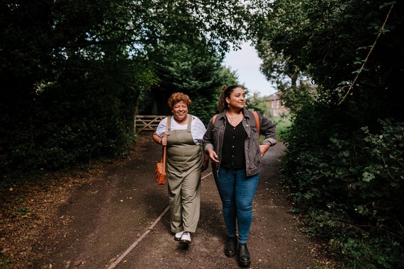 Two women in casual clothes going for a walk down a tree lined lane