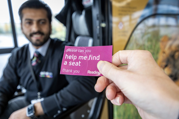 A person showing the bus driver a Safer Travel Card which says Help me find a seat
