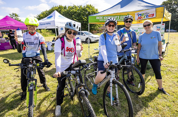four adults posing on bikes and wearing helmets, in front of the My Journey stand on the Bikeathon field at Cantley Park