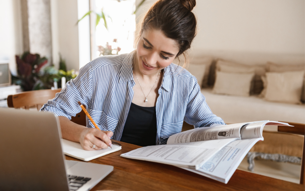 A young person studying at a desk with workbook and laptop