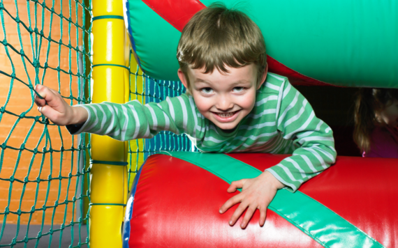 A boy squeezing through two soft rollers in a soft play area