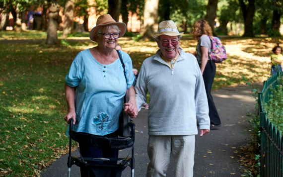 Woman with a walking aid and man smiling wearing hats in the  sunshine on a footpath