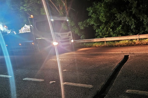 A lorry parked on a dual carriageway in the middle of the night, with its headlights on showing a section of road which has been dug up