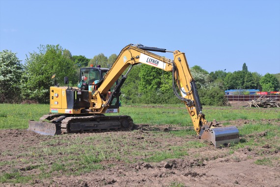 a large yellow digger sitting on churned up ground on the building site for the new road