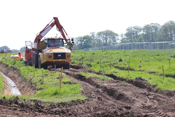 A large construction vehicle with a digger claw makes its way along a very uneven dirt track on a rural building site