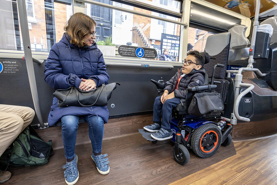 A person in a wheelchair travelling on a bus, chatting with another passenger