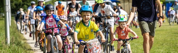 A smiling child leading a large pack of children riding toward the camera at the finish line