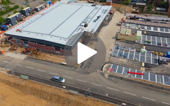aerial photo of a supermarket and car park under construction with a play button superimposed