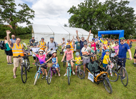 A group of adult and child cyclists gathered at the start line and cheering with hands in the air