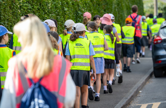 View from behind of pupils taking part in a walk along a street while wearing hi-vis jackets