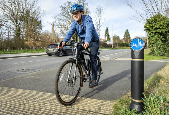 A man in a blue fleece top riding towards the camera on a cycleway beside a road